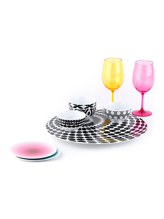 A round lazy susan with a black and white dot pattern, holding three cups, with come colorful drinkware ajacent.