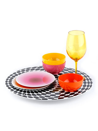 A round lazy susan with a black and white dot pattern, with colorful tableware on top..