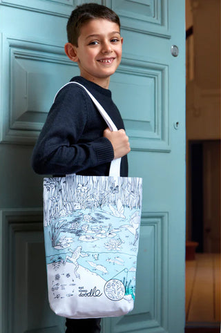 A smiling young box with a pond scene tote hanging from his shoulder.