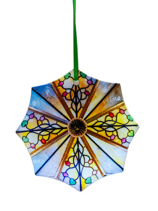 An ocatgonal stained glass ornament with a floral design, hanging from a green cord.