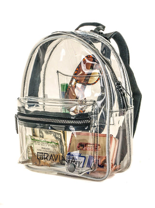 Angled view of a clear backpack with the Ravinia name and logo in its lower portion, and money, sunglasses, lip balm and a cassette tape visible inside.