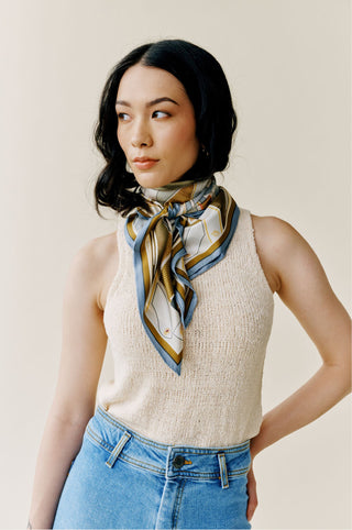 A woman in a sleeveless off-white top wearing a knotted scarf of blue, brown, khaki.