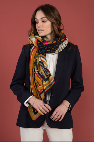 A woman in a black blazer wearing a scarf of orange, blue red, and khaki.