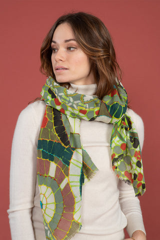 A woman wearing a scarf with nature patterns in green, red and black.