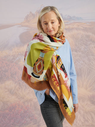 A woman wearing a blue shirt and a tan scarf with colorful details and colorful embroidery wrapped around her shoulders.