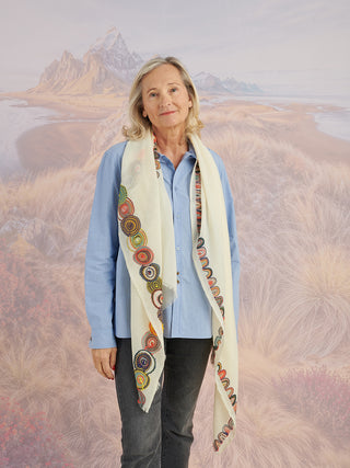 A woman wearing a blue shirt and a natural-colored scarf with a colorful embroidered border draped around her neck.