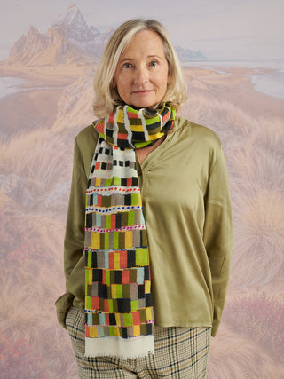 A woman wearing a green shirt and a colorful checker scarf with colorful embroidery wrapped around her neck.
