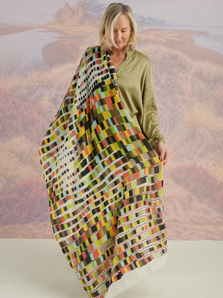 A woman with a colorful scarf with colorful embroidery draped on her shoulder, showing the full geometric pattern.