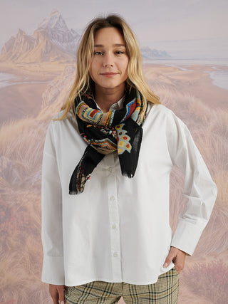 A woman wearing a black scarf with colorful embroidered details wrapped around her neck.