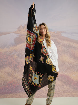 A woman holding a black scarf with colorful geometric details and colorful embroidery to show the full scarf.