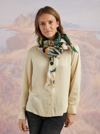 A woman wearing an ivory shirt and a teal scarf with tan, blue, and black embroidered details tied around her neck.