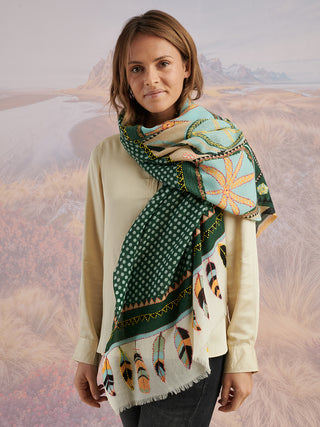A woman wearing an ivory shirt and a teal scarf with tan, blue, and black embroidered details wrapped around her neck.