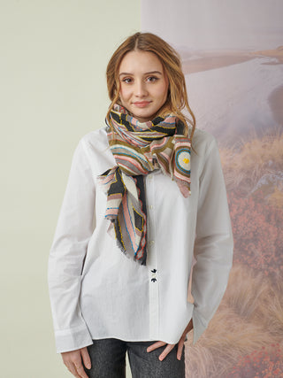 A woman wearing a white shirt and a pink, gray, and black scarf with geometric details and colorful embroidery tied around her neck.