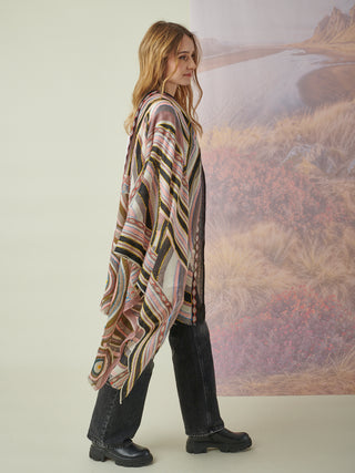 A woman with a pink, gray, and black scarf with geometric details and colorful embroidery draped over her shoulder.