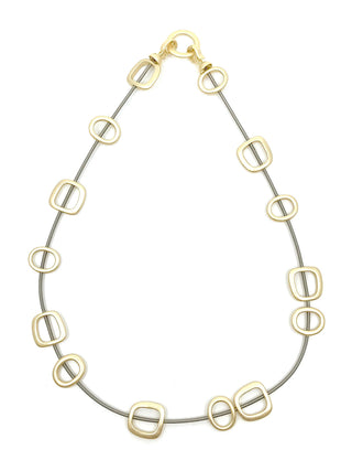 An overhead view of a piano wire necklace with gold-toned metal squares.