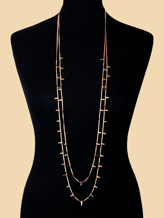 A long brass ingot necklace on a black mannequin.