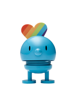 A smiling turquoise figure with a spherical head and spring in its middle, with rainbow attached to the back of its head.
