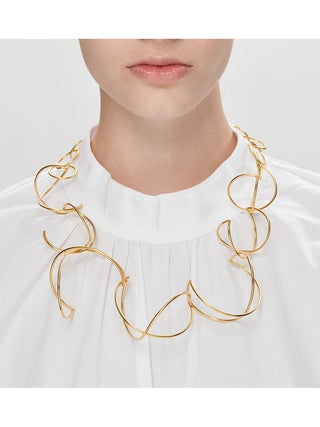 A woman in a white top wearing a brass loops necklace.