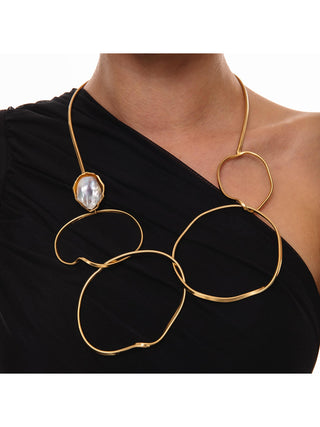 A woman in a black top wearing a brass loop necklace with a large mother of pearl piece on her right side.