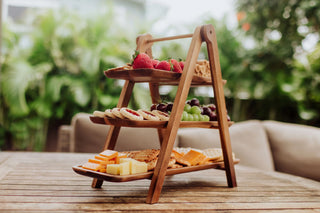 A three-tiered wooden serving ladder on a wooden table outside.