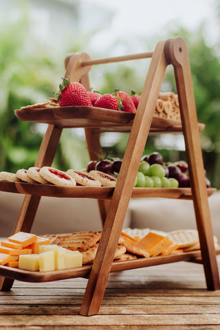 A three-tiered wooden serving ladder on a wooden table outside.
