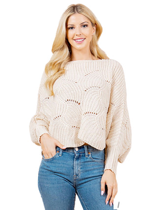 A woman wearing an ivory knit sweater poncho with blue jeans.