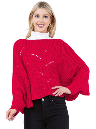 A woman wearing a red knit sweater poncho with black pants.