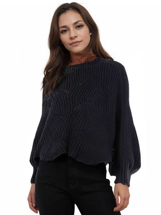 A woman wearing a black knit sweater poncho and black pants.
