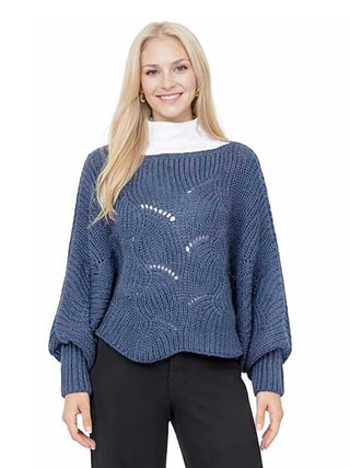 A woman wearing a dark blue knit sweater poncho and black pants.