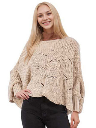 A woman wearing a light tan knit sweater poncho with black pants.
