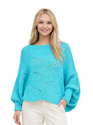 A woman wearing a turquoise knit sweater poncho and ivory pants.