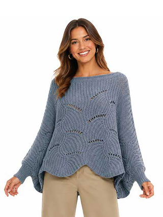 A woman wearing an light denim blue knit sweater poncho with tan pants.