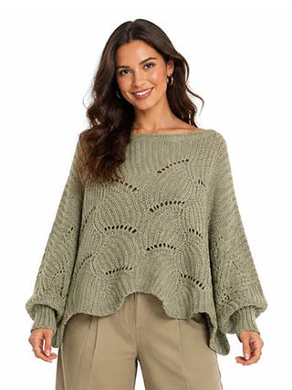 A woman wearing an sage green knit sweater poncho with tan pants.