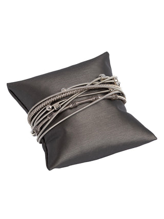 A bracelet made of several silver toned strands, adorned with various color beads, wrapped around a pillow.