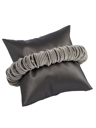 A silver-toned bracelet made of springy piano wire, wrapped around a small grey pillow.