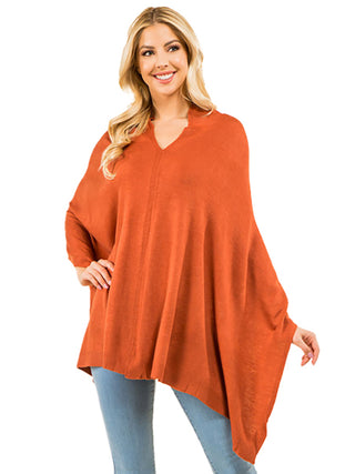A woman wearing a pumpkin colored poncho and blue jeans.