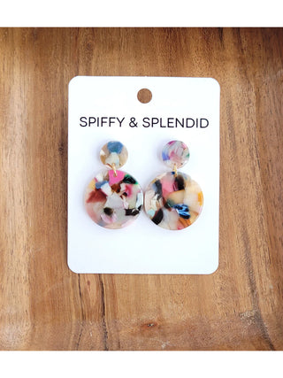 A pair of multicolored stud earrings made of two circles held together by a gold-toned clasp, displayed on a white card with the words Spiffy and Splendid on a wood background.