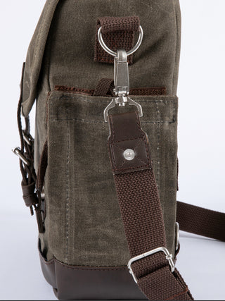 Side view of a green canvas bag, with a brown shoulder strap attached with a metal ring.