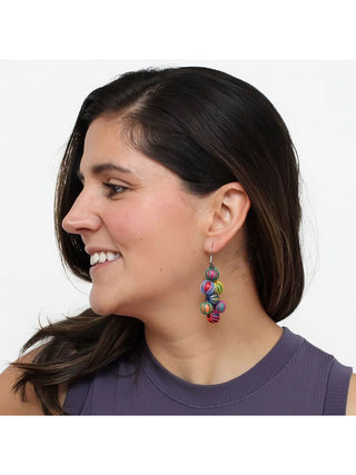 Profile view of a smiling model in a purple top wearing Earrings featuring intricately wrapped beads in a gorgeous blend of bright colors, hanging elegantly from a French wire.