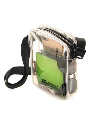Side view of a transparent brick bag with a black strap and the Ravinia logo and name in black. Inside are a green wallet, cell phone, sunglasses, and lip balm.