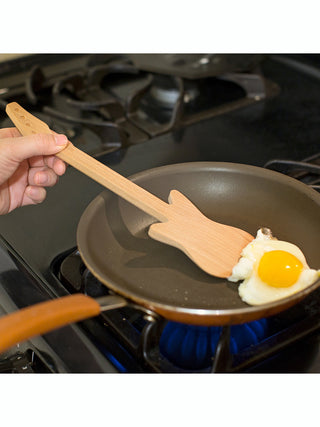 A guitar shaped wooden spatula lifting an egg in a pan.