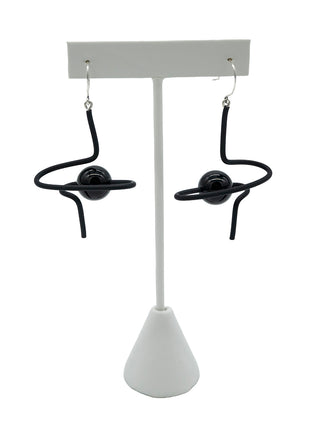 Black swirly wire earrings with a black bead, hanging on a white earring stand.