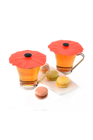 Two glasses filled with beverages and silicone poppy lids on their tops, with layered cookies adjacent.
