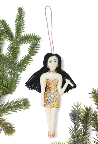 A felt ornament depicting Cher in a sequined dress, holding a microphone, surrounded by Christmas tree branches.