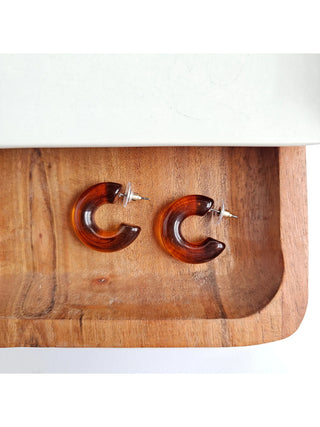A pair of brown chunky open hoop earrings with stud backings on a wooden tray.