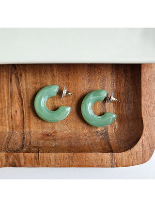 A pair of sage chunky open hoop earrings with stud backings on a wooden tray.