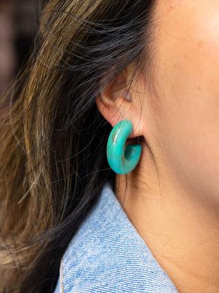 A close-up of a person wearing the turquoise Chloe hoops.