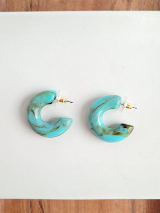 A pair of turquoise colored open hoop earrings on a white background.