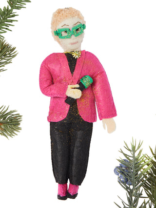 A felt ornament depicting Elton John in a glittery pink jacket, black pants, green glasses, and a sequin lapel pin, holding a microphone.