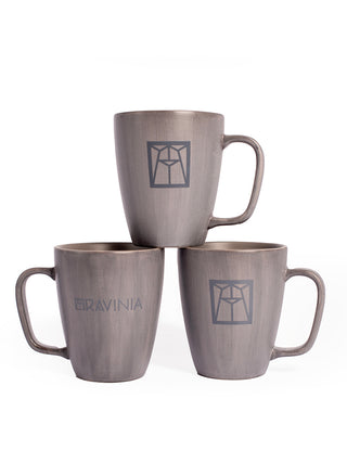 Three grey mugs, two on the bottom and one on top, the lower left one with the word Ravinia on it, and the others with the Ravinia logo in dark green.
